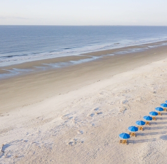 chairs with blue umbrellas lined up on a white sand beach