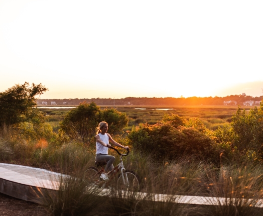 Woman biking on boardwalk with sunset