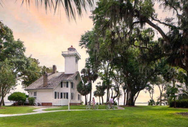 Bicyclists ride in front of a lighthouse