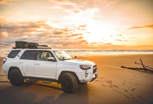 White SUV parked on beach at sunset
