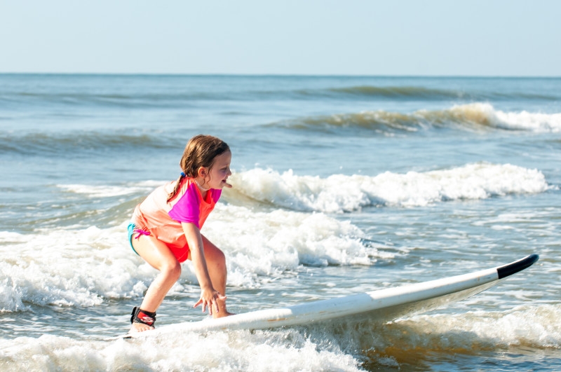 A little girl stands up on her surf board in the waves